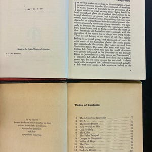 Op de afbeelding: Open boek met tekst, waaronder "Living Fossils" en een "Inhoudsopgave". Het boek is een eerste editie, gedrukt in de VS. De inhoudsopgave bevat hoofdstukken zoals "The Mysterious Spaceship."