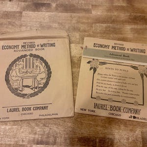May include: A vintage tan paper envelope and a matching instructional booklet titled Revised Economy Method of Writing Advanced Book by Laurel Book Company. The envelope features a circular illustration of two people writing at a desk.
