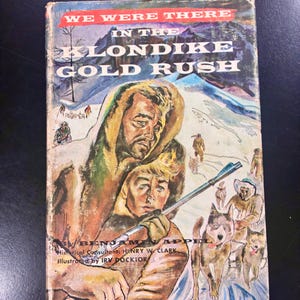 May include: Vintage book cover titled "We Were There in the Klondike Gold Rush." The cover art depicts a man and a boy in a snowy landscape, with a dog sled team and other figures. The book is illustrated by Irv Docktor.