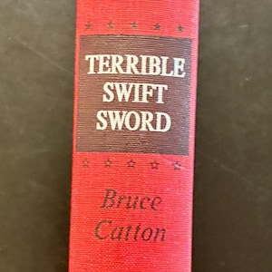 May include: A red hardcover book titled "Terrible Swift Sword" by Bruce Catton, part of "The Centennial History of the Civil War" series, published by Doubleday. The book's spine features white lettering and star accents.