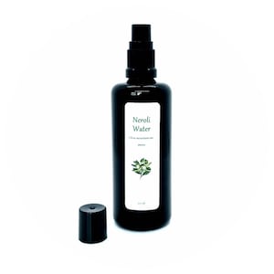 May include: A black glass bottle with a black spray nozzle and a white label that reads "Neroli Water" with the botanical name "Citrus aurantium var. amara" and a small illustration of a flower. The bottle is 100 ml.
