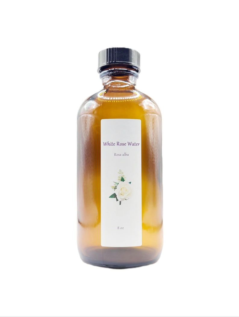 May include: A brown glass bottle of White Rose Water, with a black cap. The label features the text "White Rose Water" and "Rosa alba", along with a white rose illustration. The bottle contains 8 oz of product.