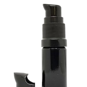 May include: A black glass bottle with a black pump top and a separate black cap. The bottle is about 5 inches tall.