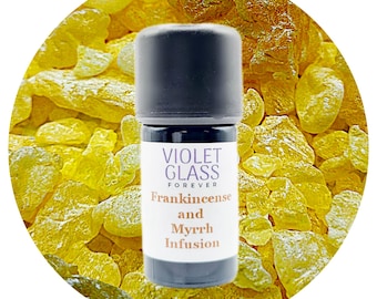 May include: A small, dark brown glass bottle with a white label that reads "VIOLET GLASS FOREVER Frankincense and Myrrh Infusion". The bottle is sitting on a bed of yellow resin crystals.