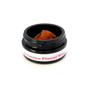 May include: A small black jar with a white label that reads "Jasmine Floral Wax". The jar contains a brown wax melt.