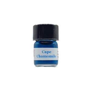 Op de afbeelding: Een klein glazen flesje met een zwarte dop gevuld met blauwe vloeistof. Het etiket vermeldt "Cape Chamomile".
