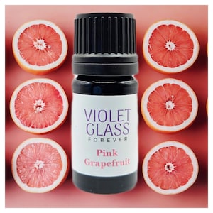 Puede incluir: Una pequeña botella de vidrio con una tapa negra y una etiqueta blanca. La etiqueta dice "Violet Glass Forever" y "Pink Grapefruit". La botella está rodeada de rodajas de pomelo rosa.