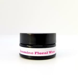 May include: A small black jar with a white label that reads "Jasmine Floral Wax".