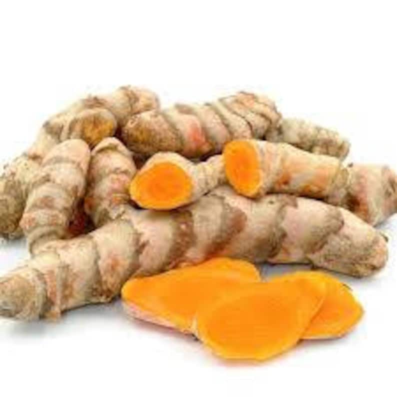 May include: A pile of turmeric root, some of which are sliced open to reveal the bright orange flesh. The root is a pale yellow color with a rough texture.