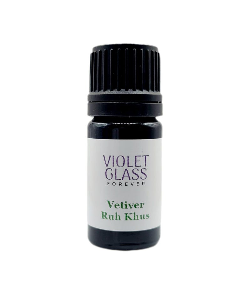 May include: A small, dark glass bottle with a black cap. The label reads "VIOLET GLASS FOREVER" and below that, "Vetiver Ruh Khus" in green text. The bottle is likely for essential oils or similar products.
