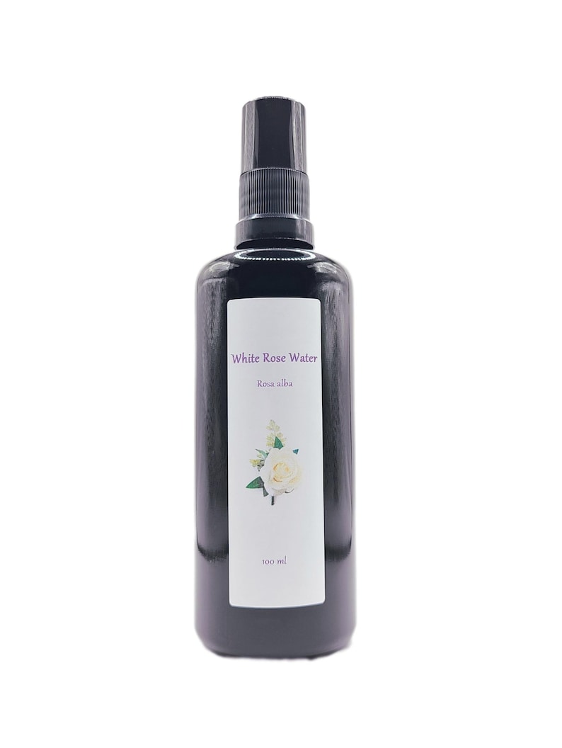 May include: A black spray bottle with a white label featuring the text "White Rose Water" and "Rosa alba." A white rose illustration is also on the label. The bottle contains 100 ml of liquid.
