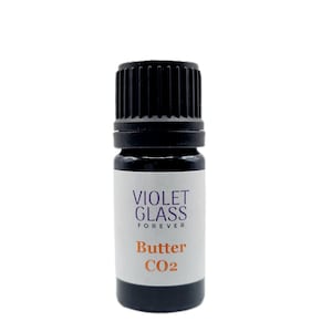 May include: A small, dark brown glass bottle with a black cap. The label reads "VIOLET GLASS FOREVER" in purple text and "Butter CO2" in orange text.