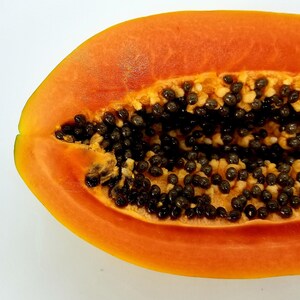 May include: A half of a ripe papaya with black seeds. The papaya is orange and has a smooth texture.