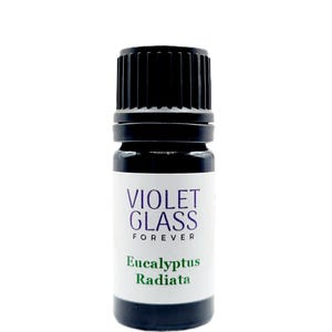Puede incluir: Una pequeña botella de vidrio marrón oscuro con una tapa de rosca negra. La etiqueta es blanca con texto morado que dice "VIOLET GLASS FOREVER" y texto verde que dice "Eucalyptus Radiata".