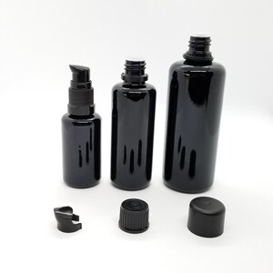 May include: Three black glass bottles with black caps and droppers. The bottles are different sizes and are arranged in a row on a white surface.