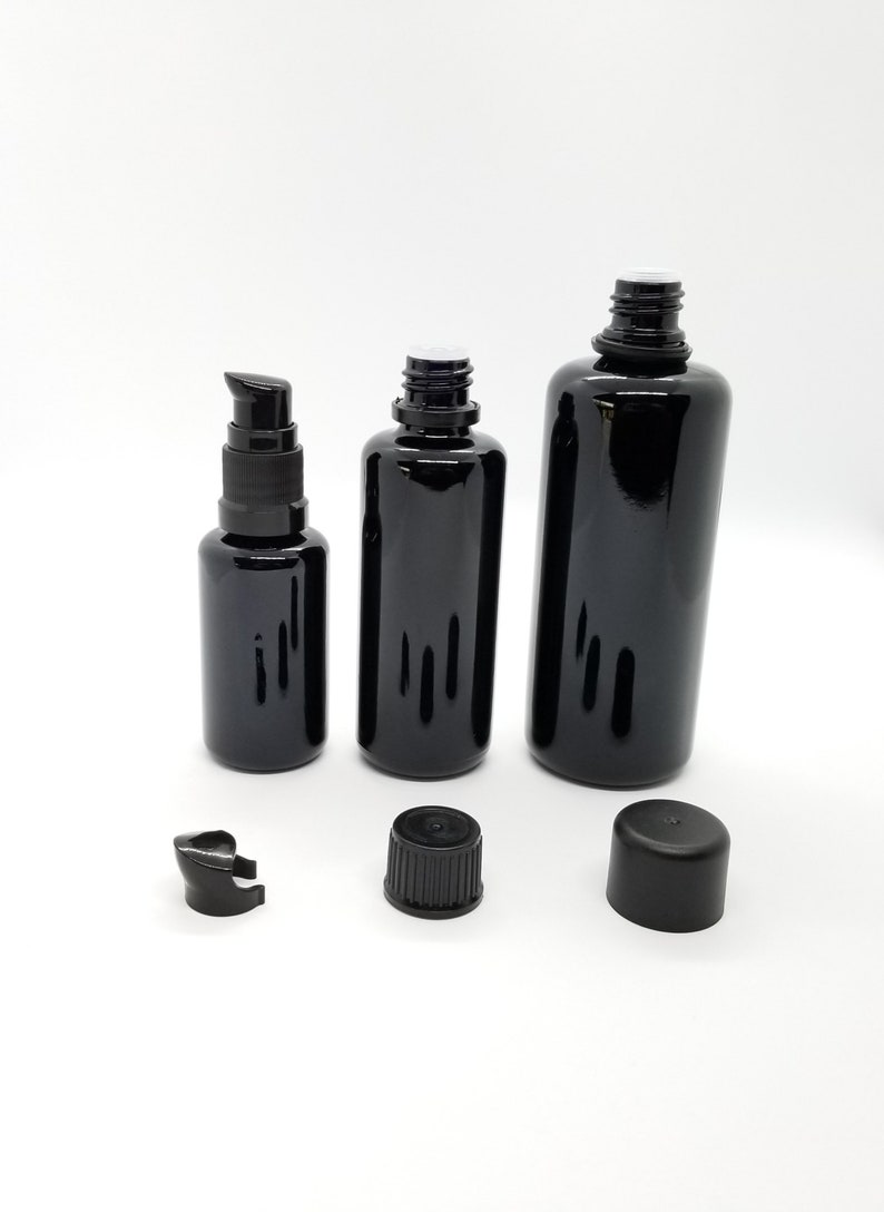 May include: Three black glass bottles with black caps and droppers. The bottles are different sizes and are arranged in a row on a white surface.