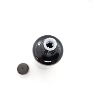 May include: A black glass bottle with a white plastic lid. The lid has a small hole in the center.