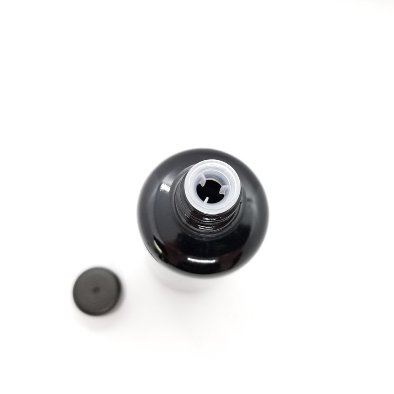 May include: A black glass bottle with a white plastic lid. The lid has a small hole in the center.