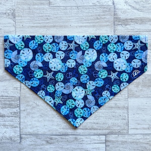 May include: A blue and white patterned dog bandana with a design of seashells and starfish.