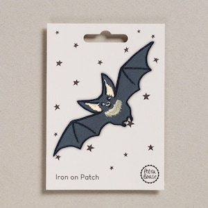 May include: A dark grey bat iron-on patch with embroidered details, including a cream-coloured chest and ears. The patch is on a white card with a star pattern and the text "Iron on Patch". The patch is from Petra Boase.