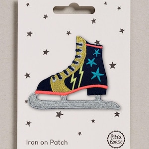 May include: An embroidered iron-on patch shaped like an ice skate. The skate is navy blue with gold accents, a neon pink trim, and three turquoise stars. A yellow lightning bolt is on the side, and the blade is silver. The text reads Iron on Patch.