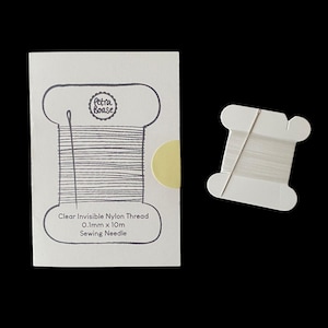 Puede incluir: Una tarjeta rectangular blanca con una ilustración impresa de un carrete con el texto Petra Boase, Clear Invisible Nylon Thread, 0.1mm x 10m, y Sewing Needle. Al lado hay un pequeño carrete de cartón blanco con hilo de nailon transparente.