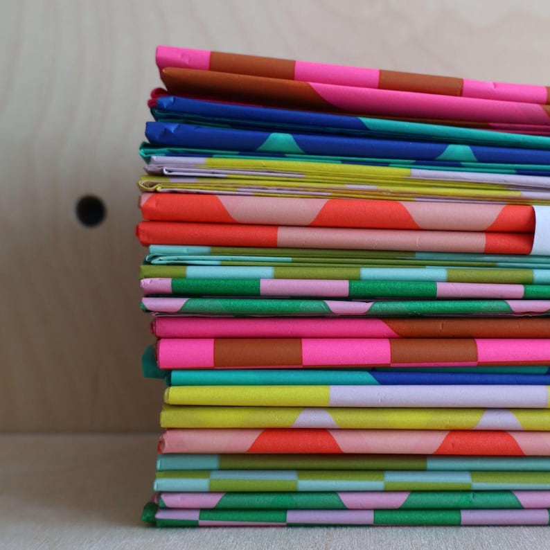 K&ouml;nnte beinhalten: Ein Stapel bunt gemusterten Papiers mit geometrischen Mustern in den Farben Rosa, Gr&uuml;n, Blau, Gelb und Orange.