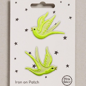 May include: Two lime green embroidered swallow bird iron-on patches displayed on a white backing card decorated with small black stars. The card features the text Iron on Patch and a circular logo with the brand name Petra Boase in black ink.