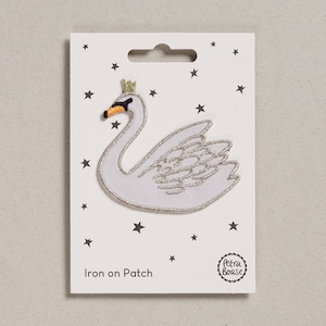 May include: White iron-on patch featuring a white swan with a gold crown. The patch is on a white card with a black star pattern and the text "Iron on Patch" and "Petra Boase".