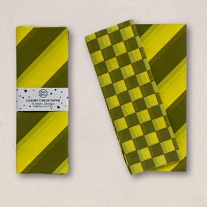 Könnte beinhalten: Eine Packung Luxus-Seidenpapier mit einem diagonalen Streifendesign in Gelb und Olivgrün. Die Packung ist mit einem weißen Band mit dem Text "LUXURY TISSUE PAPER" und dem Markennamen umwickelt. Zwei Blätter Seidenpapier werden gezeigt, eines mit einem Schachbrettmuster und das andere mit diagonalen Streifen.