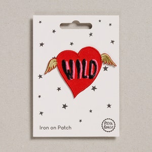 May include: A red heart-shaped iron-on patch with the word "WILD" in black and pink, gold wings, and a white background with black stars. The patch is labeled "Iron on Patch" and has a Petra Boase logo.