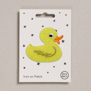 May include: A yellow duck iron-on patch with an orange beak and black eye, on a white card with black star accents. The text "Iron on Patch" is printed at the bottom. The patch is from Petra Boase.
