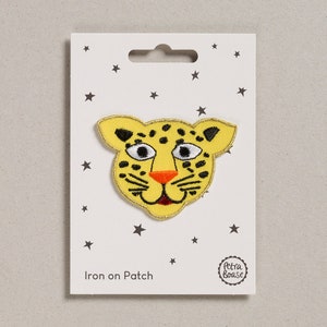 May include: Iron-on patch featuring a yellow and black cartoon leopard face with a red nose and white eyes. The patch is on a white card with the text "Iron on Patch" and a small circle with the text "Petra Boase".