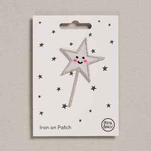 May include: White iron-on patch featuring a silver glitter star with a smiling face. The patch is displayed on a white card with black stars and the text "Iron on Patch" and a logo that reads "Petra Boase".