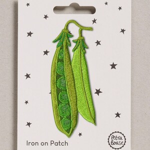 May include: An embroidered iron-on patch featuring two green pea pods on a white backing card decorated with small black stars. The text "Iron on Patch" and "Petra Boase" is printed on the card. The patch shows one open pod with peas.