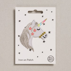 May include: Iron-on patch featuring a white unicorn with a rainbow horn and pink stars. The patch is on a white card with black stars and the text "Iron on Patch" and "Petra Boase".