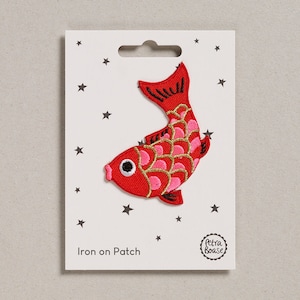 Peut inclure: Patch thermocollant rouge et rose en forme de poisson avec des écailles dorées. Le patch est sur une carte blanche avec des étoiles et le texte "Iron on Patch" et "Petra Boase".