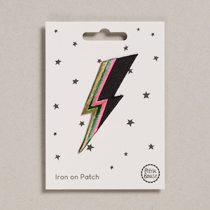 May include: Iron-on patch featuring a black lightning bolt with pink, green and gold stripes. The patch is on a white card with stars and the text "Iron on Patch" and "Petra Boase".