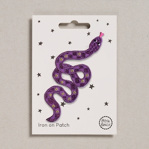 May include: Purple iron-on patch featuring a snake with a checkered pattern and gold glitter accents. The patch is on a white card with stars and the text "Iron on Patch" and "Petra Boase".
