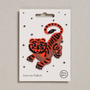 Può includere: Toppa da stirare con un tigre di cartone animato con strisce arancioni e nere. La toppa è su una carta bianca con stelle e il testo "Iron on Patch" e "Petra Boase".