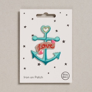 May include: An iron-on patch featuring a turquoise anchor with a pink and gold banner that says "love". The patch is on a white card with a black star pattern and the text "Iron on Patch".