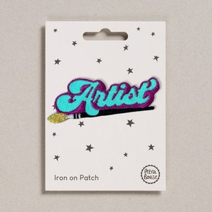 Op de afbeelding: Strijk-op patch met het woord "Artist" in turquoise blauw met een paarse omtrek en een gouden kwast eronder. De patch is op een witte kaart met sterren en de tekst "Iron on Patch".