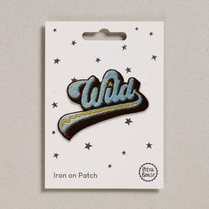 May include: Iron-on patch featuring the word "Wild" in a blue and black retro font with a gold star and a yellow lightning bolt. The patch is displayed on a white card with black stars and the text "Iron on Patch" and the Petra Boase logo.