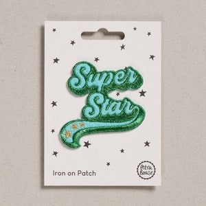 May include: Green and blue iron-on patch with the text "Super Star" in a retro font. The patch has three gold stars on a green ribbon. The patch is on a white card with black stars and the text "Iron on Patch" and "Petra Boase".