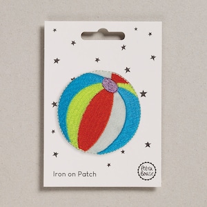 May include: Iron-on patch featuring a colourful beach ball with red, yellow, blue and white stripes. The patch is on a white card with stars and the text "Iron on Patch" and "Petra Boase".