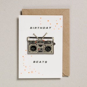 May include: A white card with the words "Birthday Beats" and a silver and black boombox with orange stars in the background.