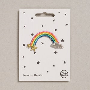 Op de afbeelding: Strijk-op patch met een regenboog, een wolk en twee gouden sterren. De patch is op een witte kaart met een zwart sterrenpatroon en de tekst "Iron on Patch" en "Petra Boase".
