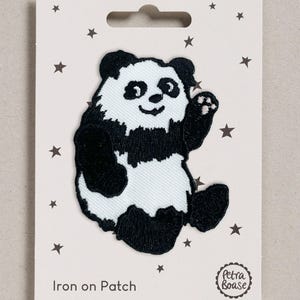 May include: An embroidered iron-on patch featuring a black and white panda bear waving its paw. The patch is attached to a white backing card decorated with small dark stars and the text "Iron on Patch" and "Petra Boase" in a circular logo.