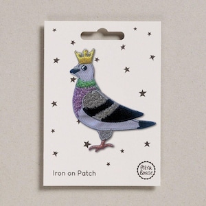 May include: An iron-on patch depicting a cartoon pigeon wearing a gold crown. The pigeon has a purple chest, grey wings, and black and grey stripes. The patch is on a white card with black stars and the text "Iron on Patch".
