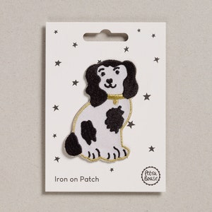 Può includere: Toppa da stirare con un cane bianco e nero con un collare dorato. La toppa è su una carta bianca con stelle nere e il testo "Iron on Patch" e "Petra Boase".